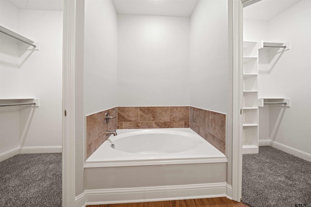 bathroom featuring a walk in closet, baseboards, and a bath