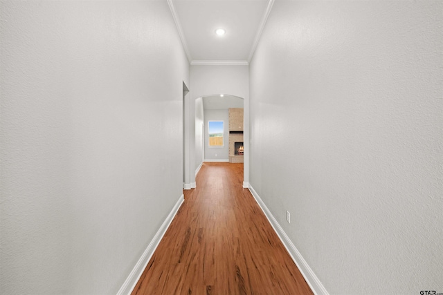 corridor featuring arched walkways, baseboards, ornamental molding, and wood finished floors