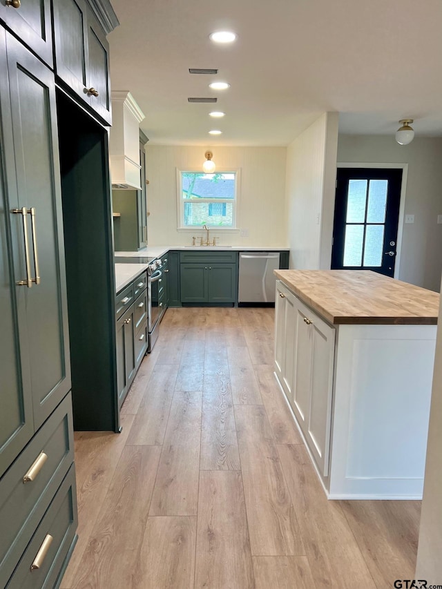 kitchen with a sink, stainless steel appliances, light wood-style floors, a center island, and wooden counters