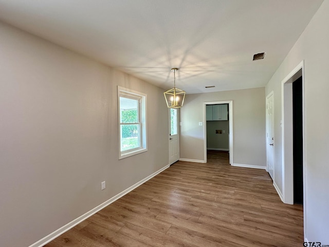 unfurnished dining area with wood finished floors, a chandelier, and baseboards