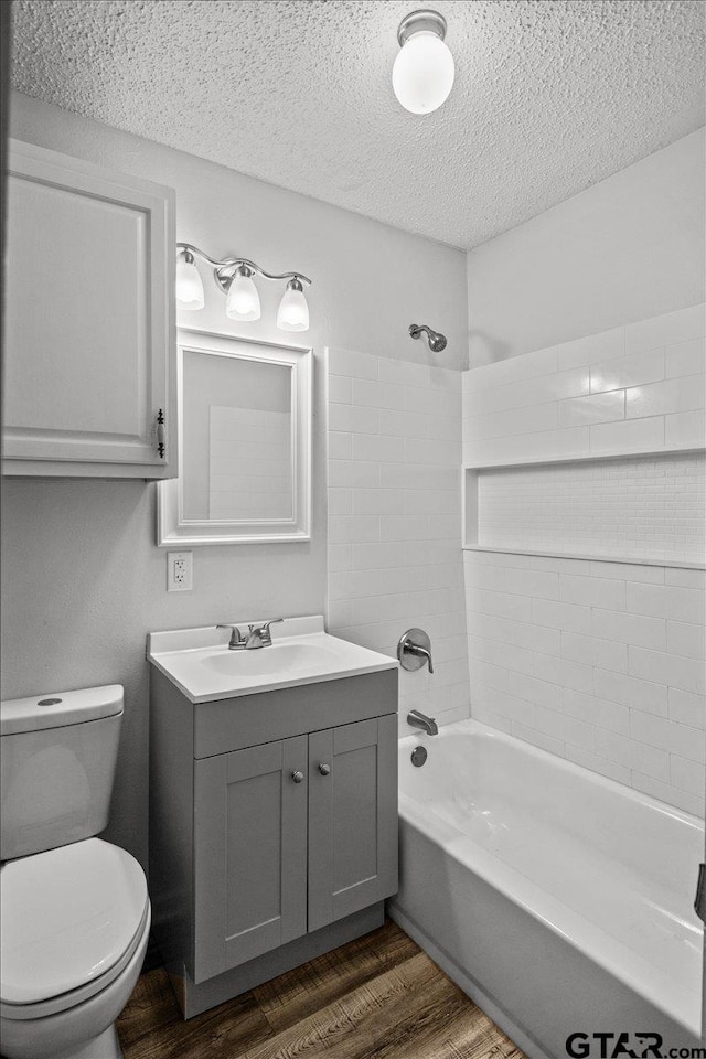 full bathroom featuring tiled shower / bath, a textured ceiling, wood-type flooring, vanity, and toilet