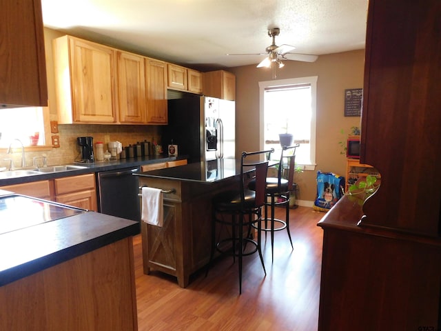 kitchen featuring dishwashing machine, a sink, dark countertops, fridge with ice dispenser, and tasteful backsplash