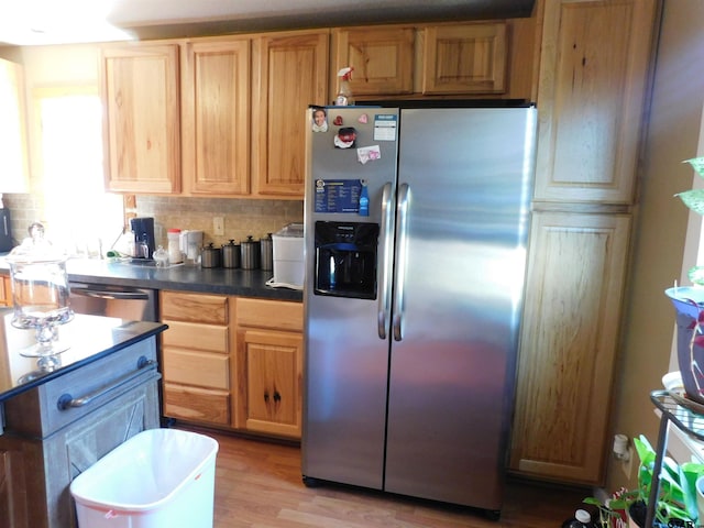 kitchen featuring dark countertops, light brown cabinetry, light wood-type flooring, decorative backsplash, and appliances with stainless steel finishes