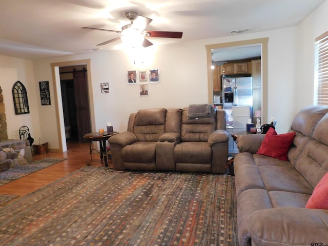 living area featuring visible vents, a ceiling fan, a barn door, and wood finished floors