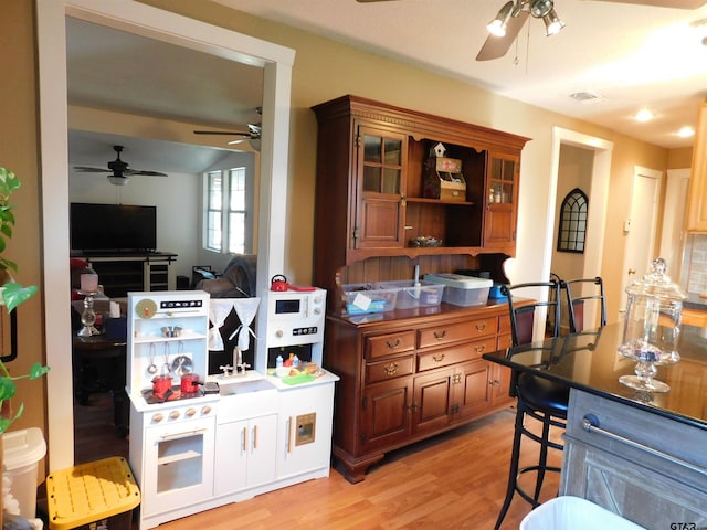 kitchen with ceiling fan, visible vents, a kitchen breakfast bar, and light wood-style flooring