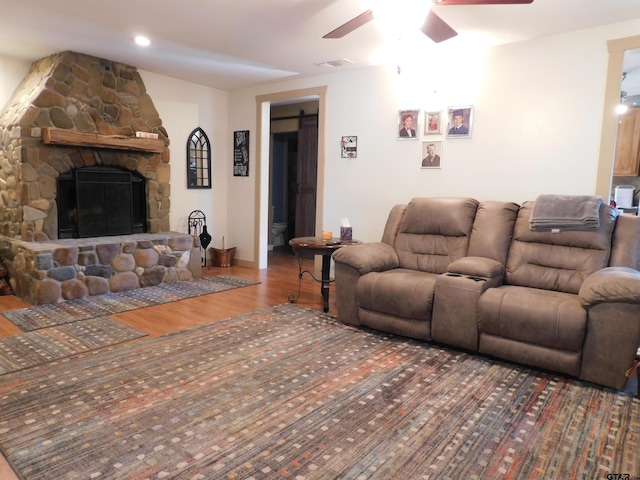 living area featuring baseboards, a barn door, a fireplace, wood finished floors, and a ceiling fan