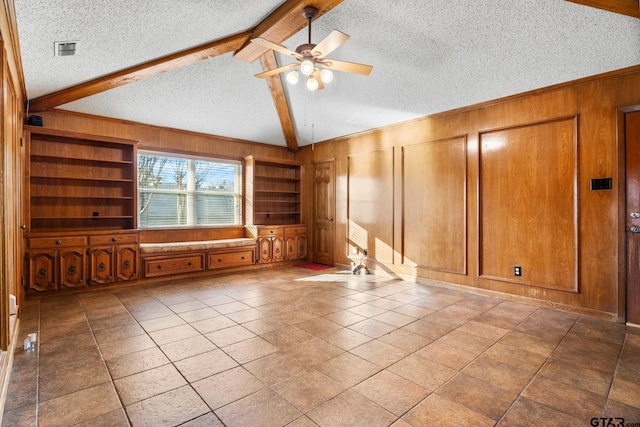 unfurnished living room with wooden walls, vaulted ceiling with beams, tile patterned flooring, ceiling fan, and a textured ceiling