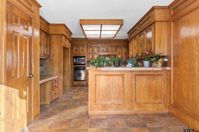 kitchen featuring tile countertops, stainless steel appliances, kitchen peninsula, and a textured ceiling