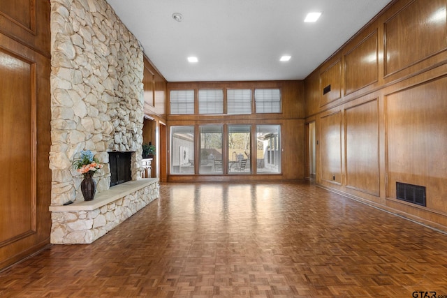 unfurnished living room featuring parquet floors, wooden walls, a stone fireplace, and a high ceiling