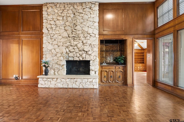 unfurnished living room with dark parquet flooring, a stone fireplace, a healthy amount of sunlight, and wooden walls