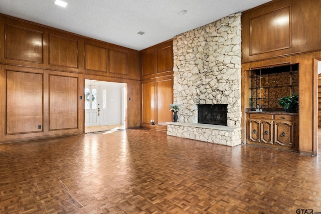 unfurnished living room with dark parquet flooring, wooden walls, and a textured ceiling