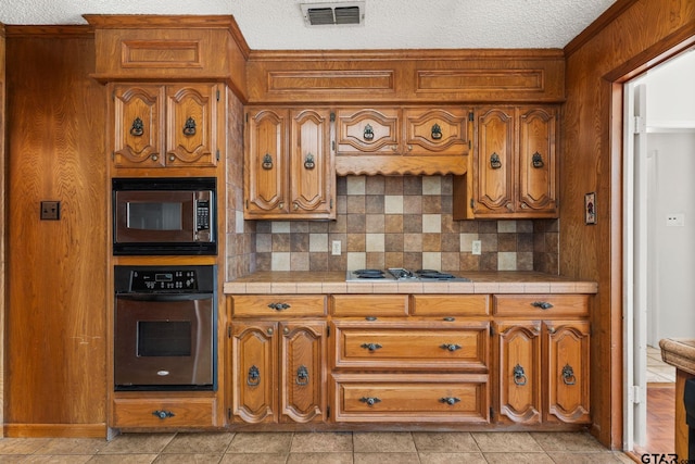 kitchen with stainless steel appliances, tile countertops, a textured ceiling, and backsplash