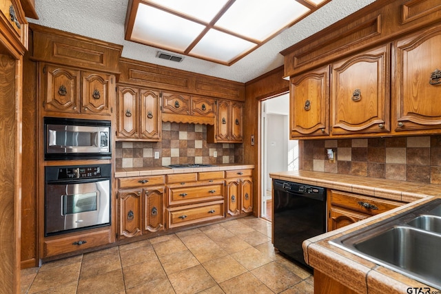 kitchen with sink, light tile patterned floors, tile counters, stainless steel appliances, and decorative backsplash