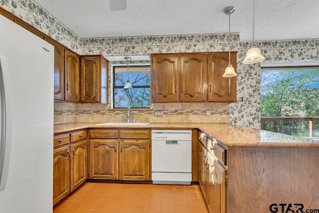 kitchen featuring sink, white appliances, decorative light fixtures, and a textured ceiling