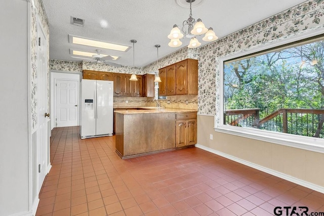 kitchen with a skylight, white refrigerator with ice dispenser, a textured ceiling, decorative light fixtures, and tile patterned floors