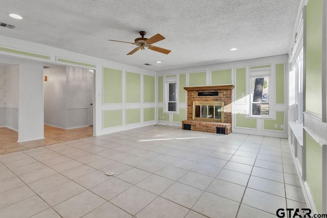 unfurnished living room with a brick fireplace, light tile patterned floors, a textured ceiling, and ceiling fan