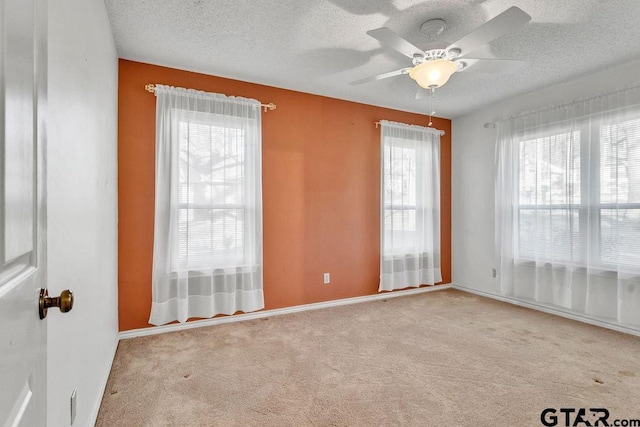 empty room with ceiling fan, light colored carpet, a textured ceiling, and a wealth of natural light