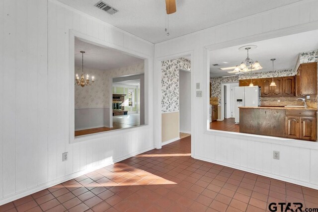 kitchen with white refrigerator with ice dispenser, sink, ceiling fan with notable chandelier, and decorative light fixtures