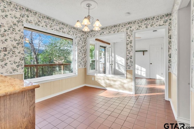 unfurnished dining area with tile patterned floors, a chandelier, and a textured ceiling