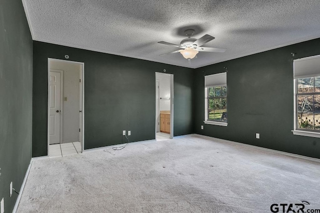 unfurnished bedroom with multiple windows, ensuite bathroom, light colored carpet, and ceiling fan