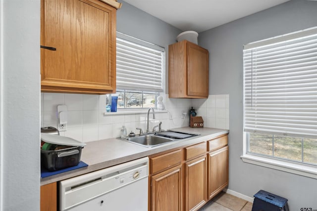 kitchen featuring backsplash, light countertops, light tile patterned floors, white dishwasher, and a sink