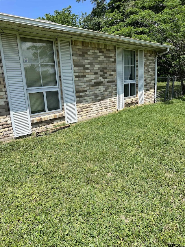 view of property exterior with a lawn, brick siding, and fence