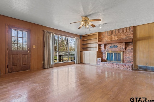 unfurnished living room featuring built in shelves, wood walls, a textured ceiling, and a wealth of natural light