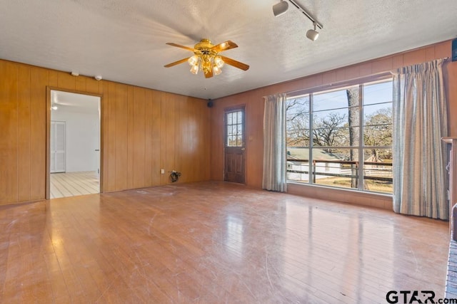 unfurnished room with a textured ceiling, wooden walls, and a healthy amount of sunlight