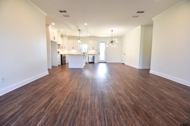 unfurnished living room with sink, a notable chandelier, crown molding, and dark wood-type flooring