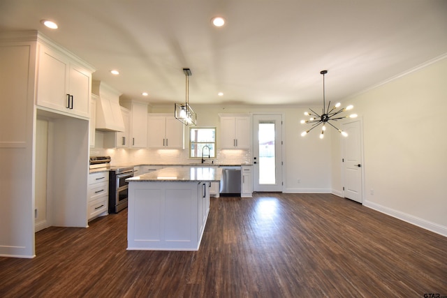 kitchen with premium range hood, stainless steel appliances, sink, white cabinets, and a kitchen island