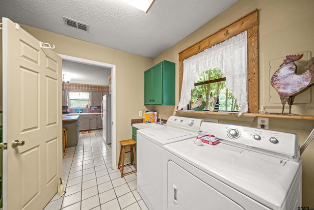 laundry room with washing machine and clothes dryer, cabinets, a textured ceiling, and light tile patterned floors