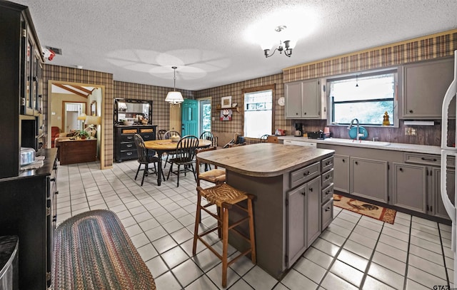 kitchen with light tile patterned flooring, sink, a center island, gray cabinets, and pendant lighting