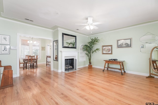 living room with light wood-type flooring, ceiling fan with notable chandelier, and ornamental molding