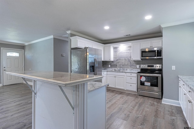 kitchen featuring white cabinets, a kitchen breakfast bar, light hardwood / wood-style flooring, appliances with stainless steel finishes, and a kitchen island