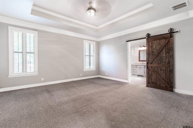 empty room with ornamental molding, a barn door, a raised ceiling, and carpet floors