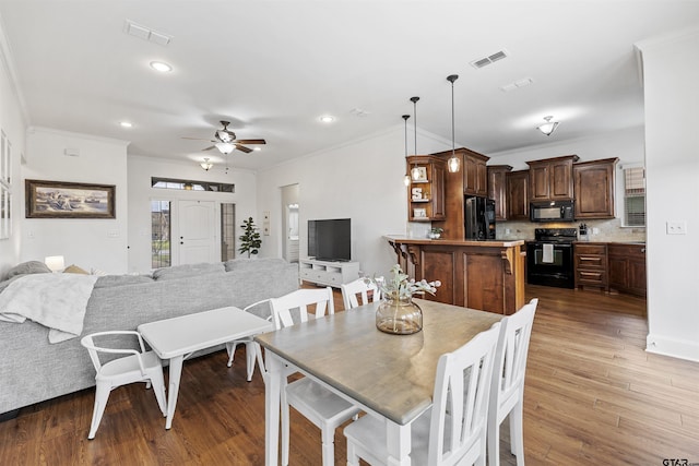 dining area with crown molding, a ceiling fan, visible vents, and dark wood-style floors