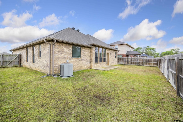 rear view of property with brick siding, a fenced backyard, central AC, and a yard