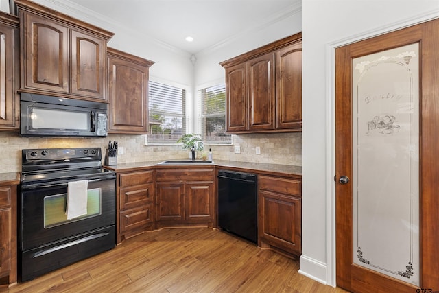 kitchen with crown molding, backsplash, black appliances, and light wood-type flooring