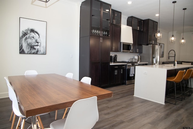 kitchen featuring a center island with sink, appliances with stainless steel finishes, decorative light fixtures, a kitchen breakfast bar, and dark wood-type flooring