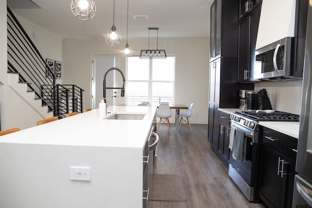 kitchen with stainless steel appliances, dark hardwood / wood-style floors, sink, and a kitchen island with sink