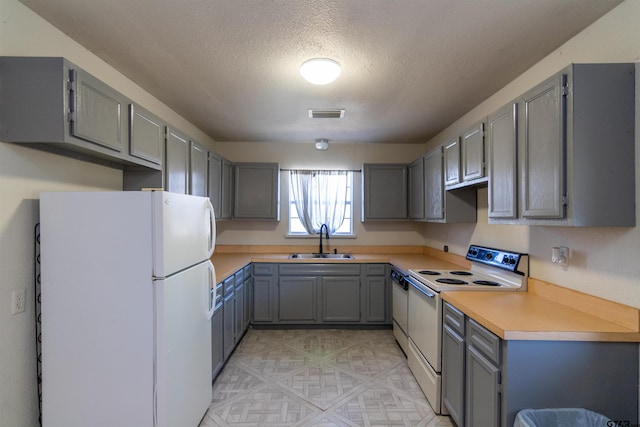 kitchen with light countertops, visible vents, gray cabinetry, a sink, and white appliances