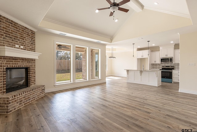 unfurnished living room featuring sink, ceiling fan, crown molding, light wood-type flooring, and lofted ceiling with beams