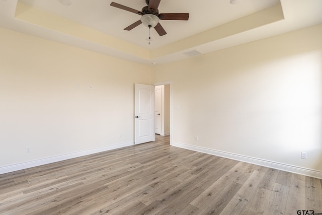 spare room featuring ceiling fan, light wood-type flooring, and a tray ceiling