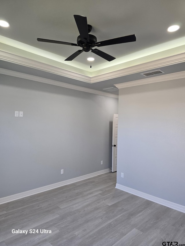 empty room featuring crown molding, light hardwood / wood-style floors, a raised ceiling, and ceiling fan