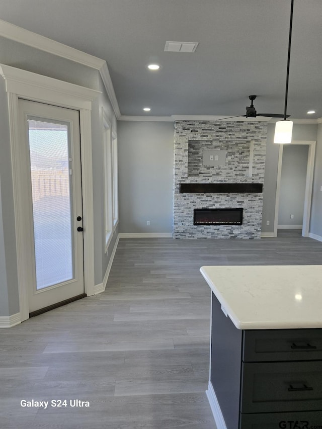 kitchen featuring crown molding, ceiling fan, hanging light fixtures, light hardwood / wood-style floors, and a stone fireplace