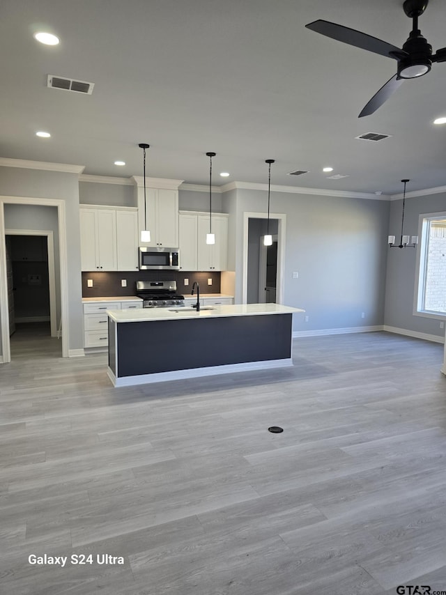 kitchen featuring crown molding, stainless steel appliances, white cabinets, and a center island with sink