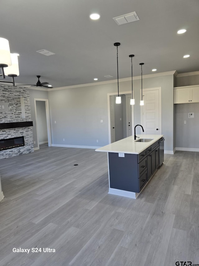 kitchen with sink, crown molding, a kitchen island with sink, white cabinetry, and decorative light fixtures