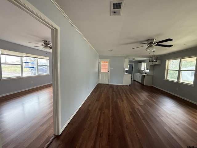 unfurnished living room featuring dark wood-style floors, a healthy amount of sunlight, visible vents, and crown molding