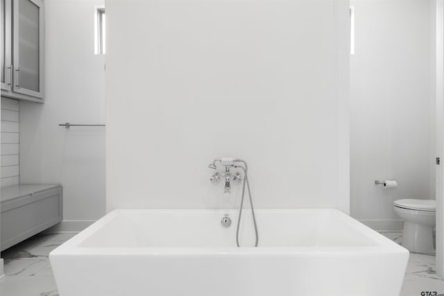 4645 Cascades Blvd, Tyler, TX 75709 - bathroom featuring marble look tiles, toilet, a tub to relax in, and baseboards