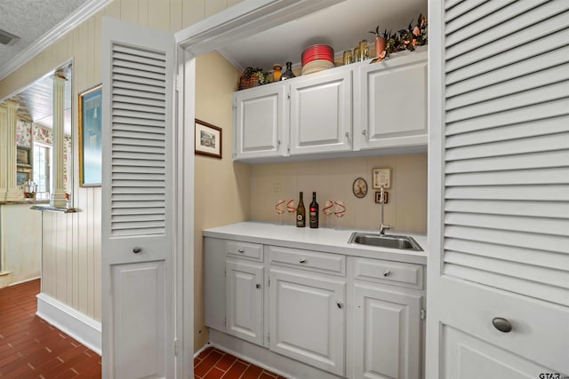 bar with crown molding, sink, white cabinets, and a textured ceiling